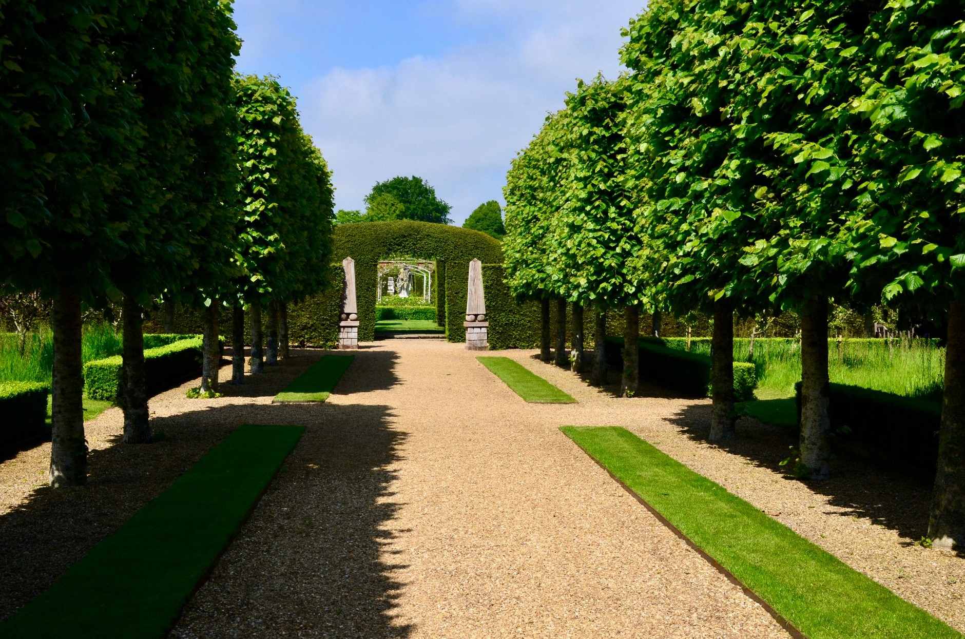 A picturesque garden pathway flanked by symmetrical trees and hedges under a clear sky.