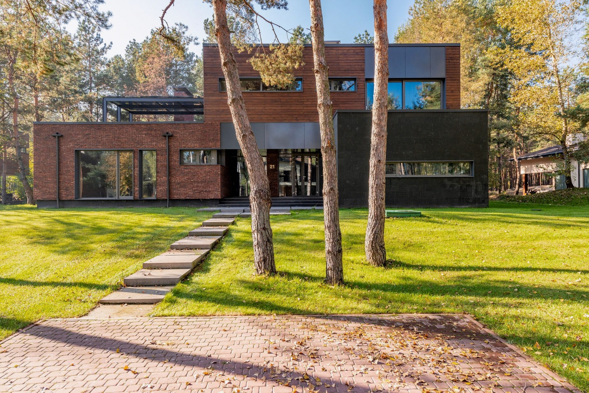 Contemporary house with large glass windows surrounded by lush greenery and a paved pathway.