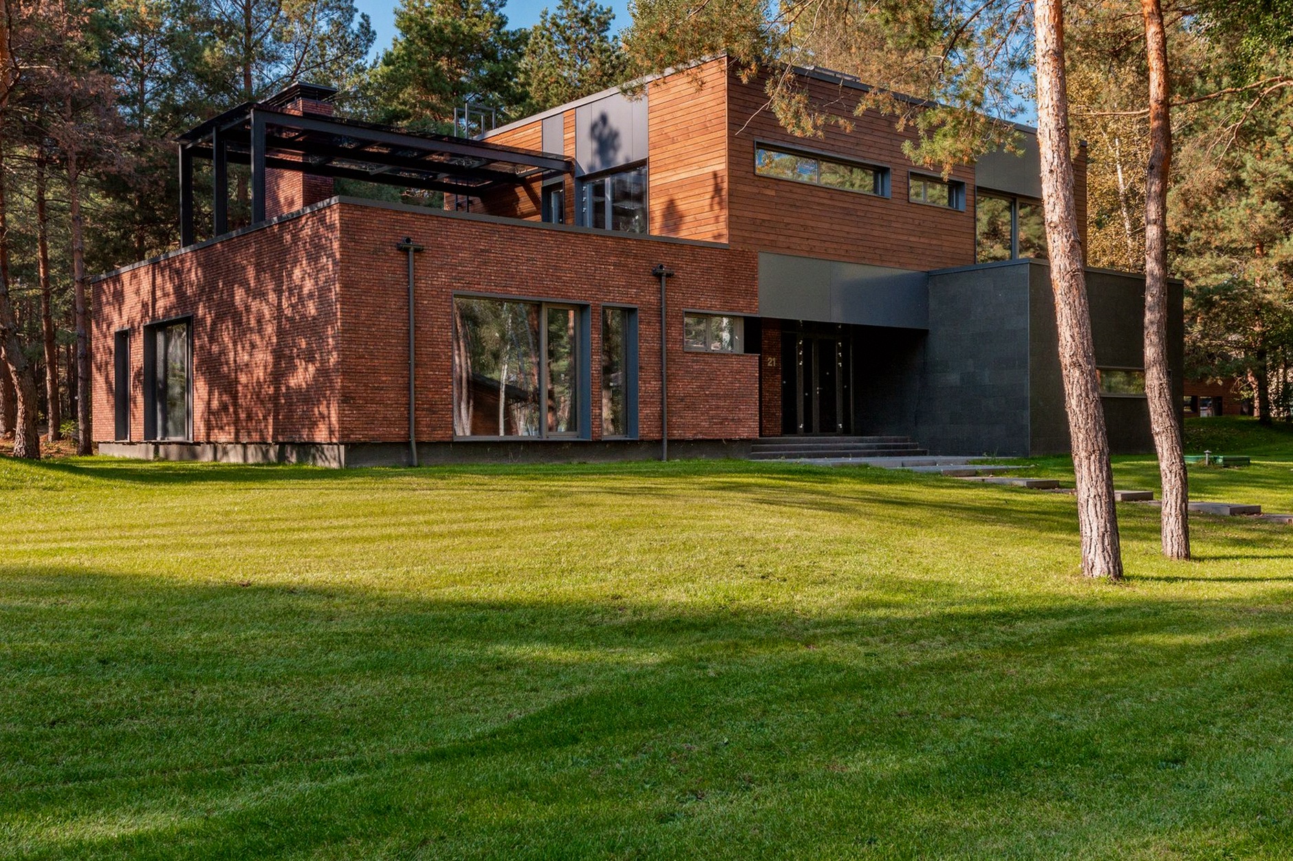 Contemporary house with large windows surrounded by lush greenery and trees.